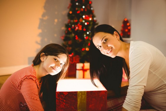 Madre e hijas sentadas al lado de un árbol de navidad y un regalo abierto