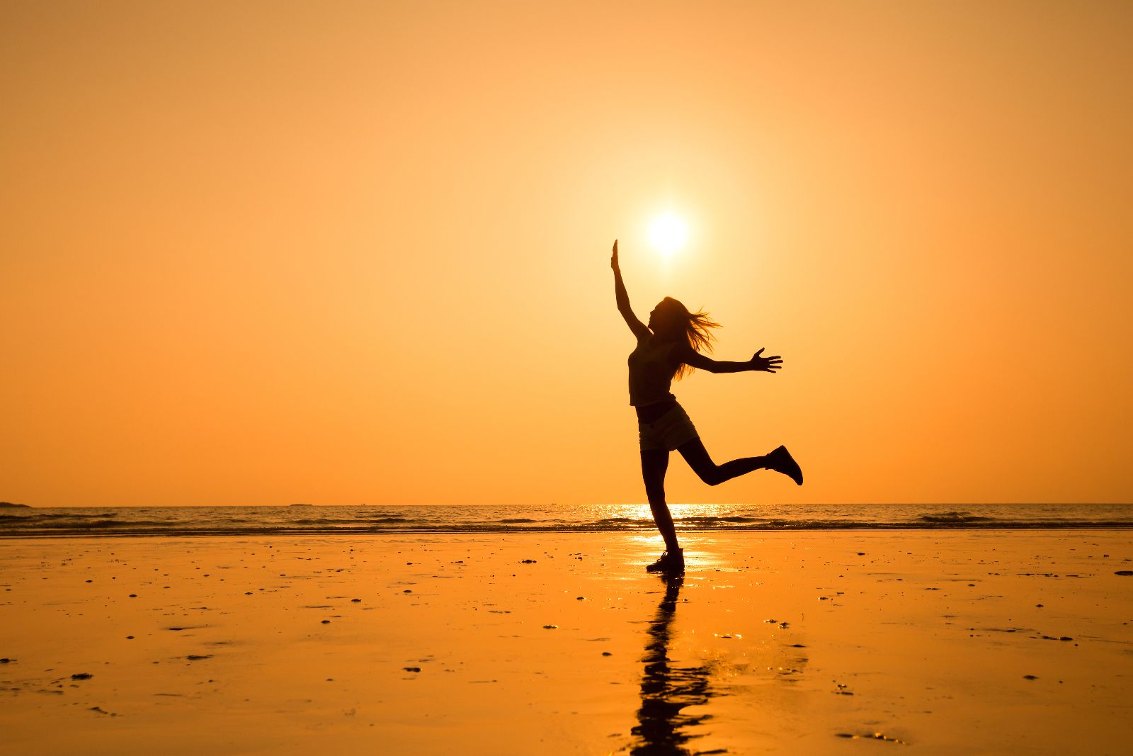 Silueta de una niña en una playa con un atardecer naranja