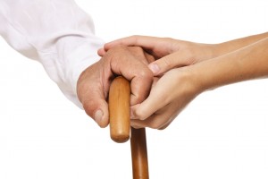 Acercamiento a las manos de un adulto mayor steniendo un bastón cin la mano de una mujer agarrándole la mano