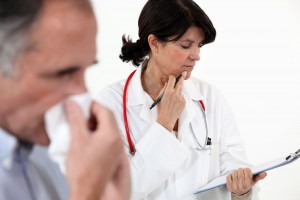 Paciente se tapa la nariz, al fondo una doctora revisa una tabla