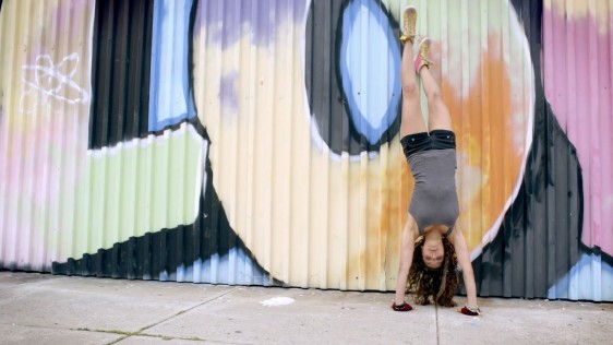 Mujer parada en sus manos al lado de un graffiti