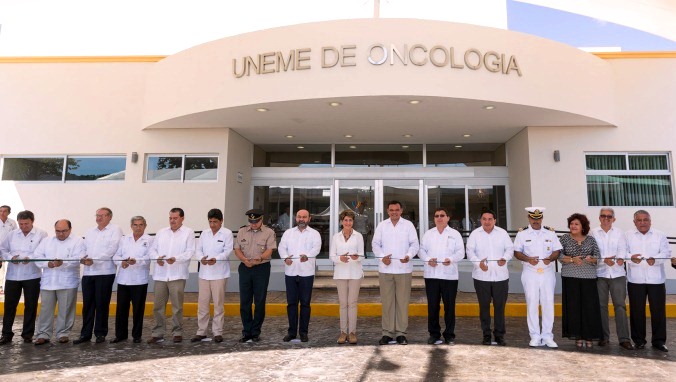 Funcionarios de pie cortando listón en la fachada de la UNEME en Oncología