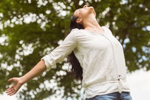 Mujer con brazos abiertos y mirando hacia un cielo azul al fondo arboles