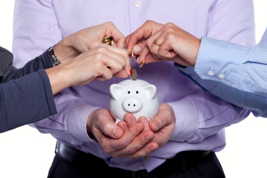 Personas depositando una moneda en una alcacía en forma de cochinito