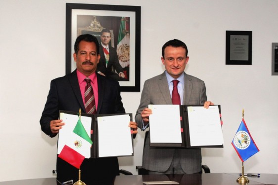 De izquierda a derecha Pablo Marín y Mikel Arriola sotienen un documento al lado de las banderas de México y Belice y al fondo la fotografía de Enrique Peña Nieto con la banda presidencial de México