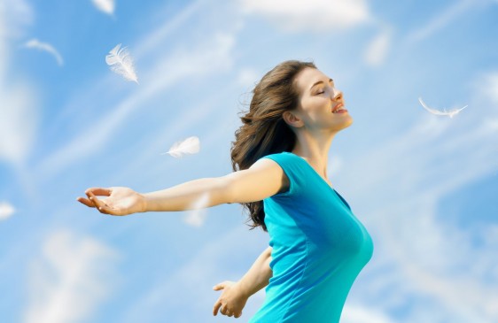 Mujer con los brazos abiertos y ojos cerrados respirando en un cielo azul