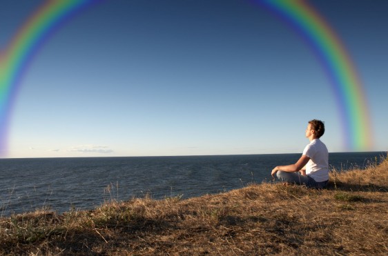 Mujer mirando al mar con un arco iris