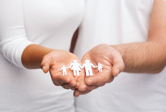 Una pareja con camisas blancas sostiene en las manos un recorte de papel que representa una famila familia