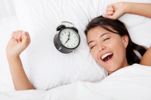Mujer despertando con un reloj al lado de su almohada