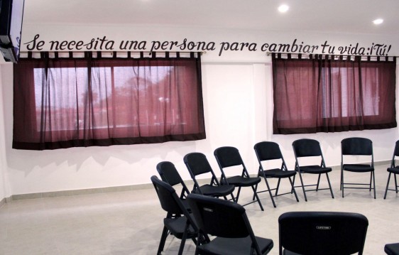 Sala con sillas en la parte superior del muro con ventanas se lee el texto "Se necesita una persona para cambiar tu vida: ¡Tú!"