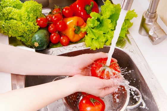 Acercamiento a las manos de una mujer lavanado con agua verduras