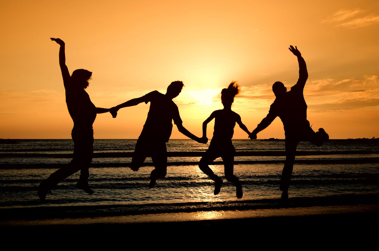 Grupo de hombres y mujeres saltando en un amanecer naranja