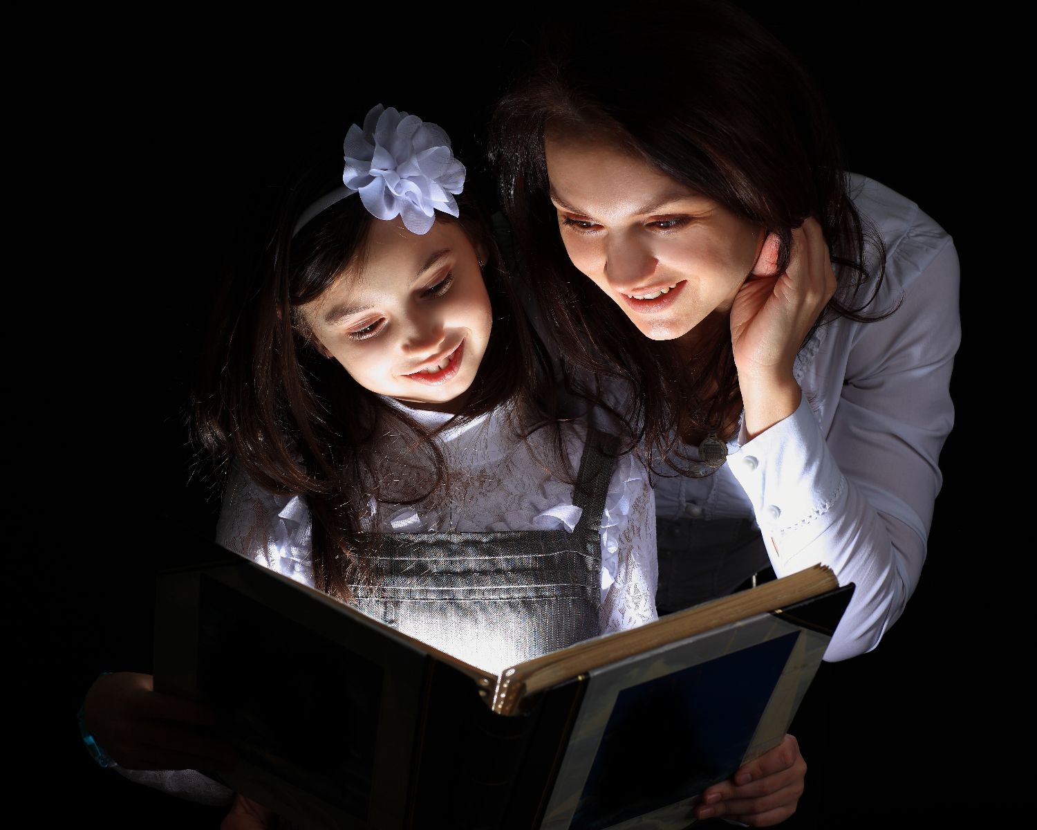 Madre e hia leyendo en un libro que emite una luz
