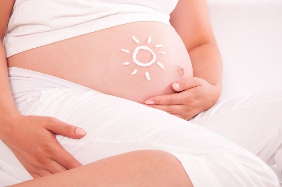 Mujer embarazada con crema olar en la barriga en forma de sol