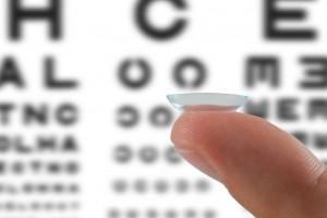 Acercamiento a lente de contacto sostenido en un dedo al fondo una prueba de la vista