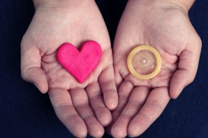 Manos de una mujer mostrando un corazón y en la otra un condón