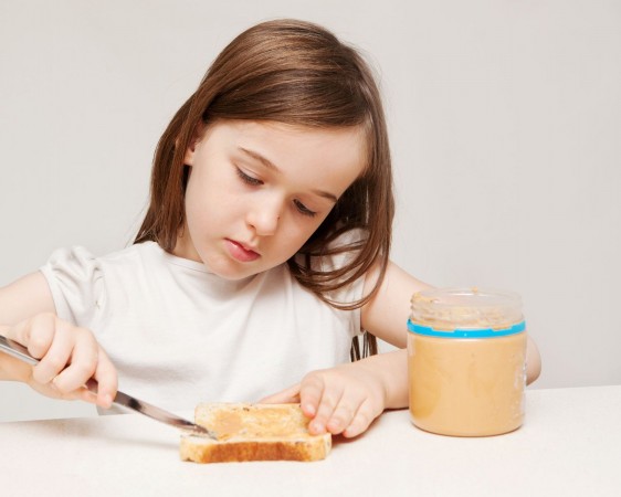 A young girl spreads peanut butter onto a piece of wholemeal bread.