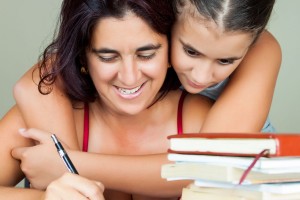Mujer estudiando en casa mientras su hija la abraza por detrás