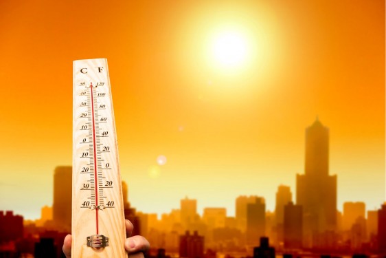 termómetro de mano muestra alta temperatura al fondo una ciudad con un sol