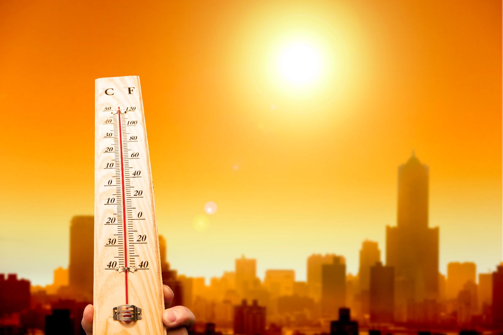 termómetro de mano muestra alta temperatura al fondo una ciudad con un sol