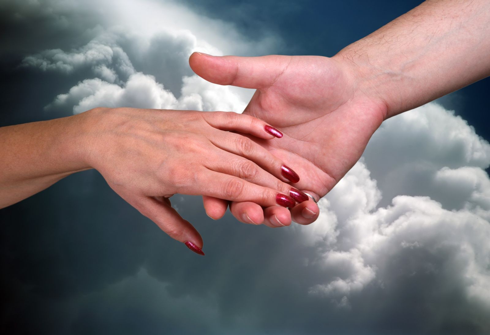 La mano de una mujer alcanzando la mano de un hombre al fondo un cielo nublado