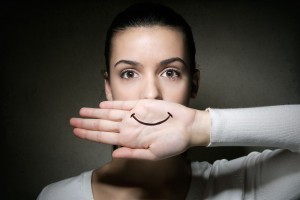 Mujer tapandose la boca con la mano en donde esta dibujada una sonrisa