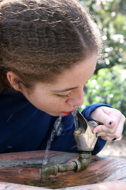 Niña con camisa azul bebiedo agua en un bebedero