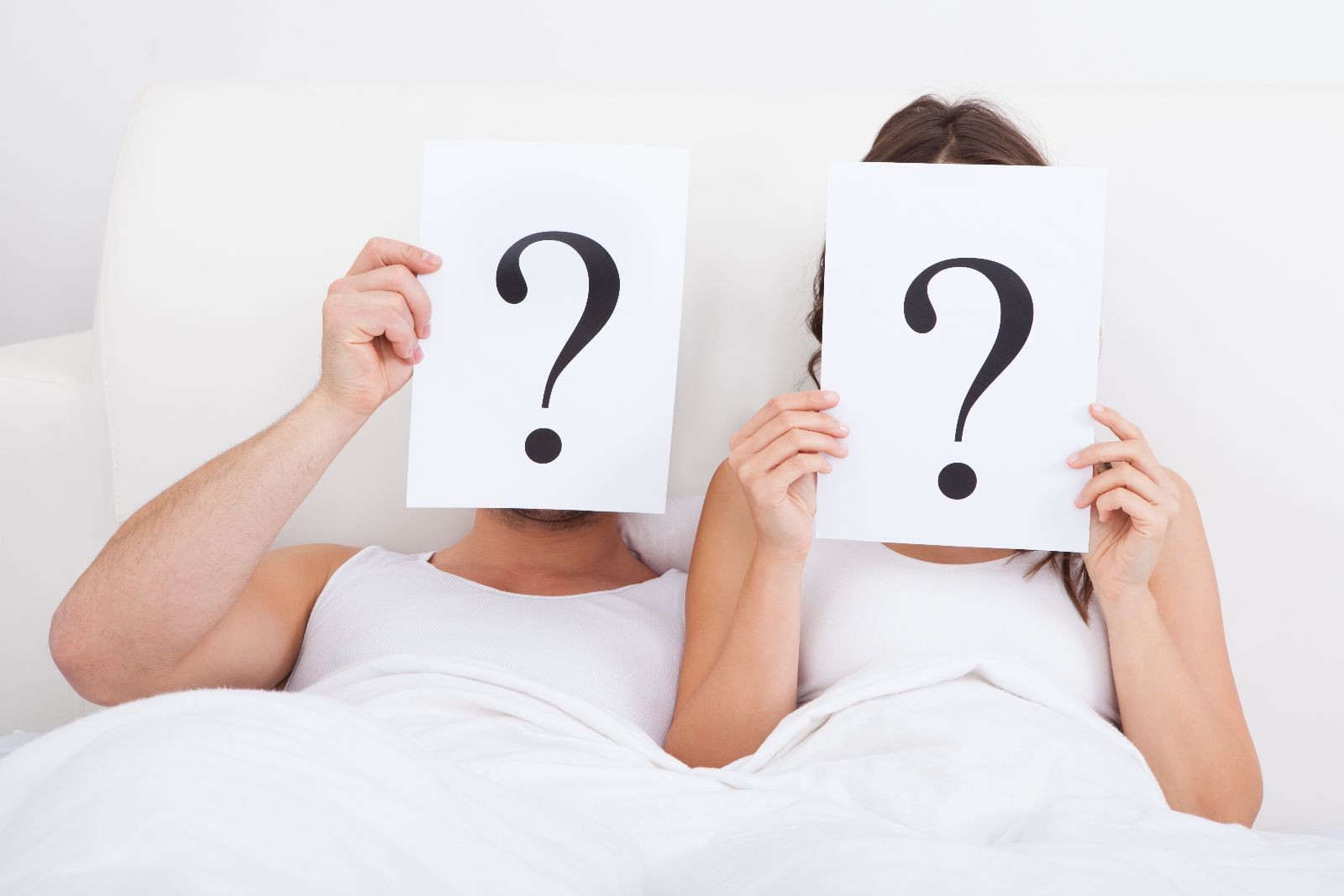 pareja en una cama mostrando signos de interrogación