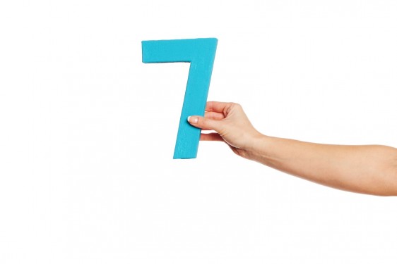 Mano de una mujer que sostiene un número siete azul en un fondo blanco