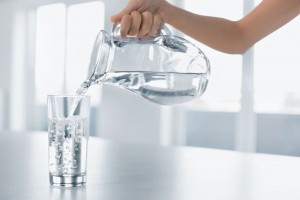 mujer sirviendo un vaso de agua desde una jarra de cristal