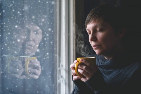 Mujer con una taza en la mano viendo nevar