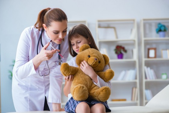 Doctora examinando a niña con un oso de peluche