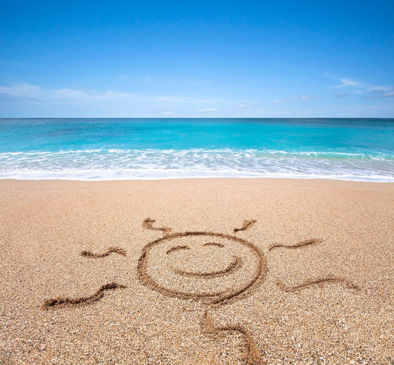 Panorámica de una playa con un dibujo de sol sonriente en la arena