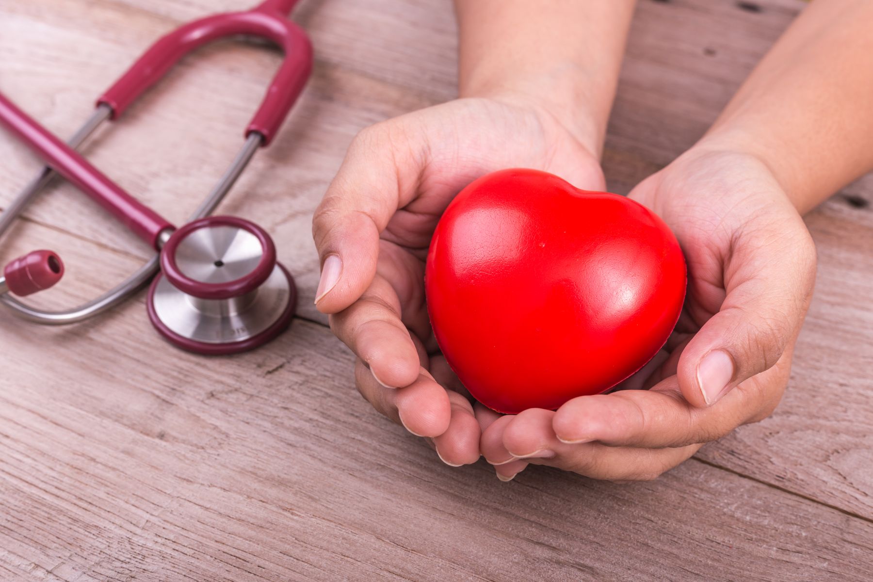 Manos sostienen un corazón en una mesa con un estetoscopio