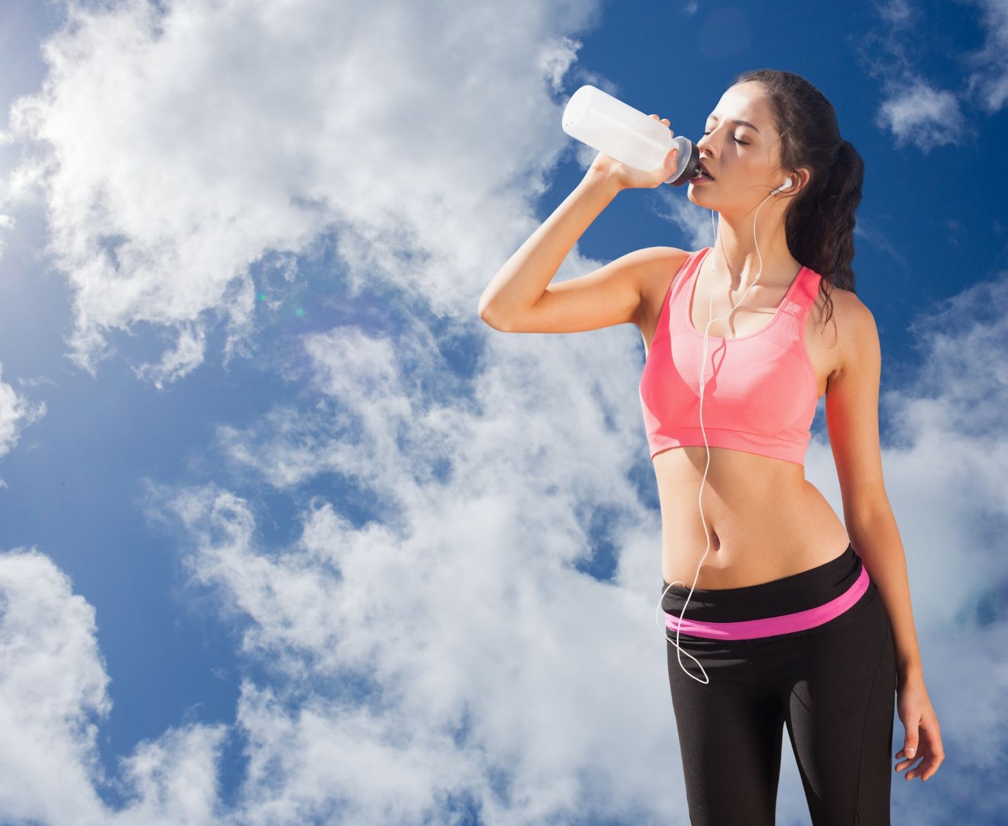 mujer en ropa deportiva tomando agua al fondo un cielo azul con nubes