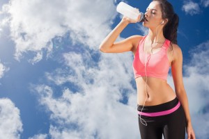 mujer en ropa deportiva tomando agua al fondo un cielo azul con nubes