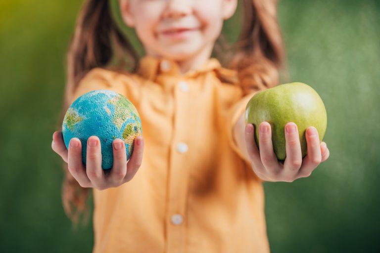 Niña que sostiene el modelo globo y manzana sobre fondo borroso, concepto de día de la tierra