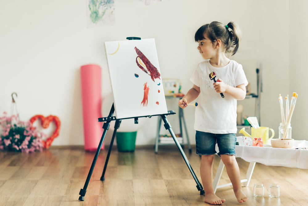 Niña en casa pintando en caballete.