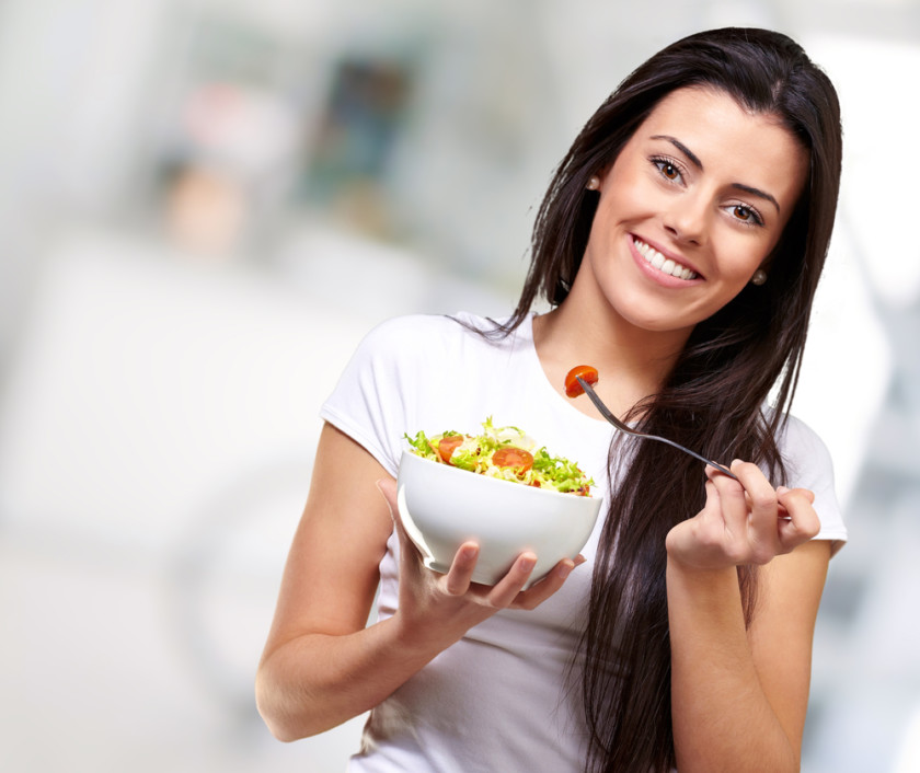 mujer joven comiendo ensalada de verduras y sonriendo