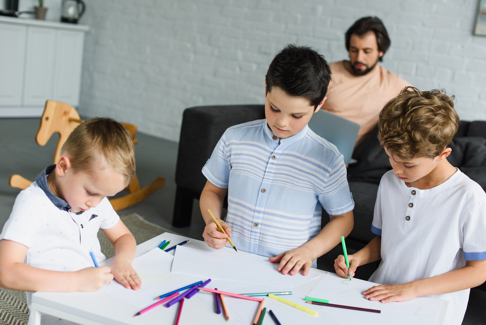 Niños y papá en casa realizando varias actividades como dibujar y leer