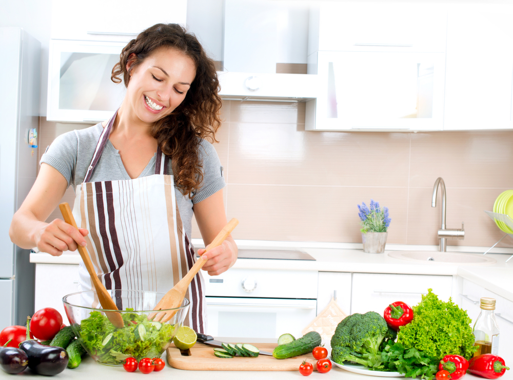 Joven contenta cocinando verduras en la cosina