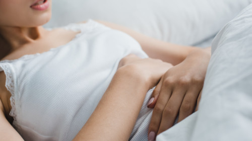Mujer joven recostada en su cama abrazando su abdomen con gesto de dolor