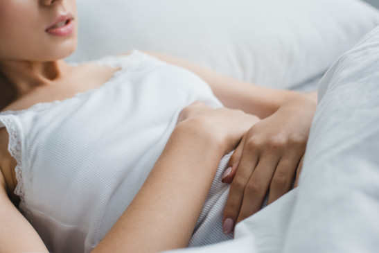 Mujer joven recostada en su cama abrazando su abdomen con gesto de dolor