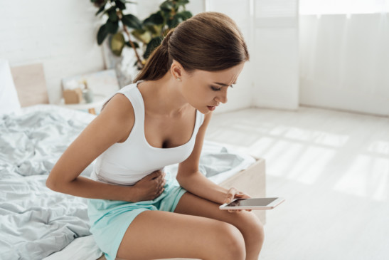 chica sentada sobre la cama con dolor de cólicos