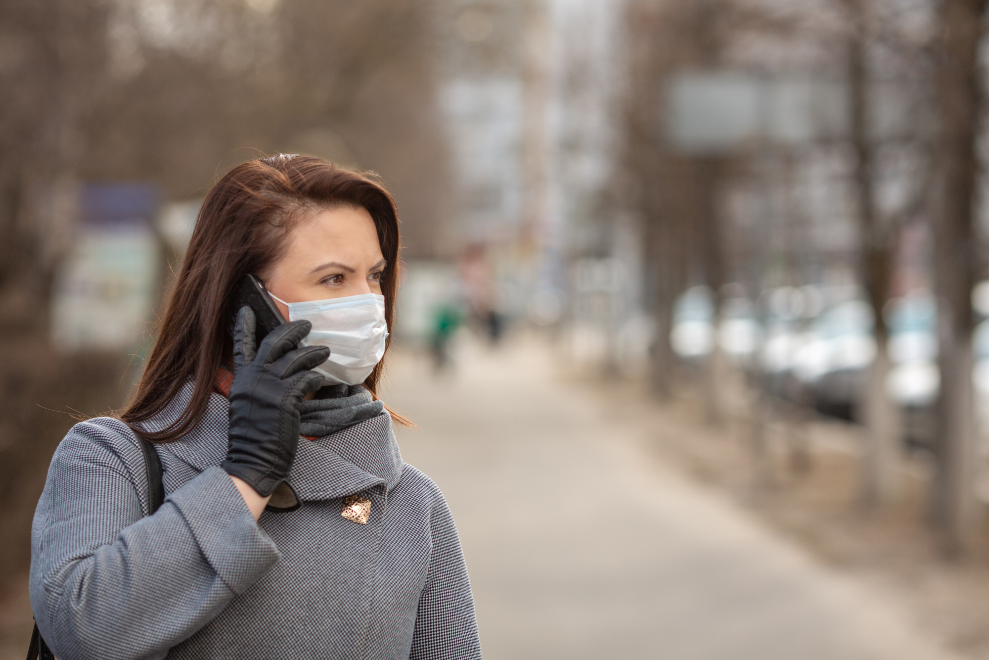 Mujer que lleva máscara médica protectora una calle vacía, al aire libre. Mujer que tiene un teléfono. Concepto de autoasistencia