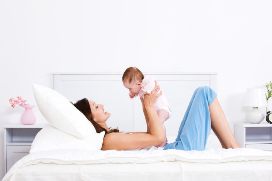 Mamá feliz acostada en el sillón alzando a su bebé en brazos