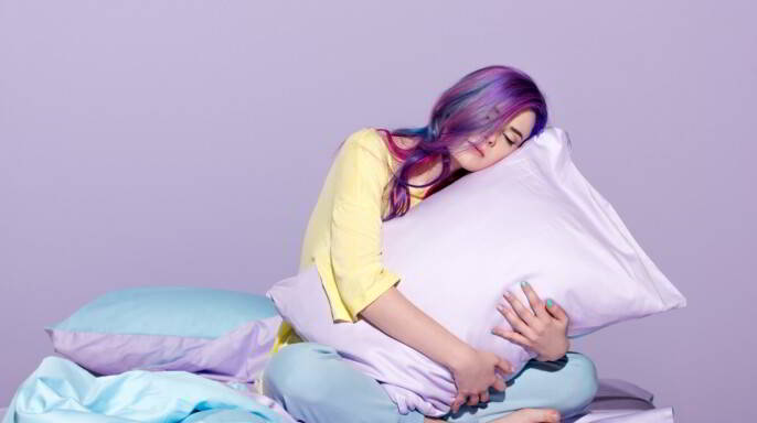 joven sentada en la cama y abrazando una almohada