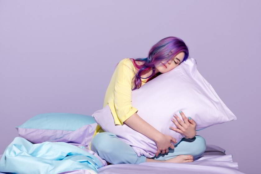 joven sentada en la cama y abrazando una almohada