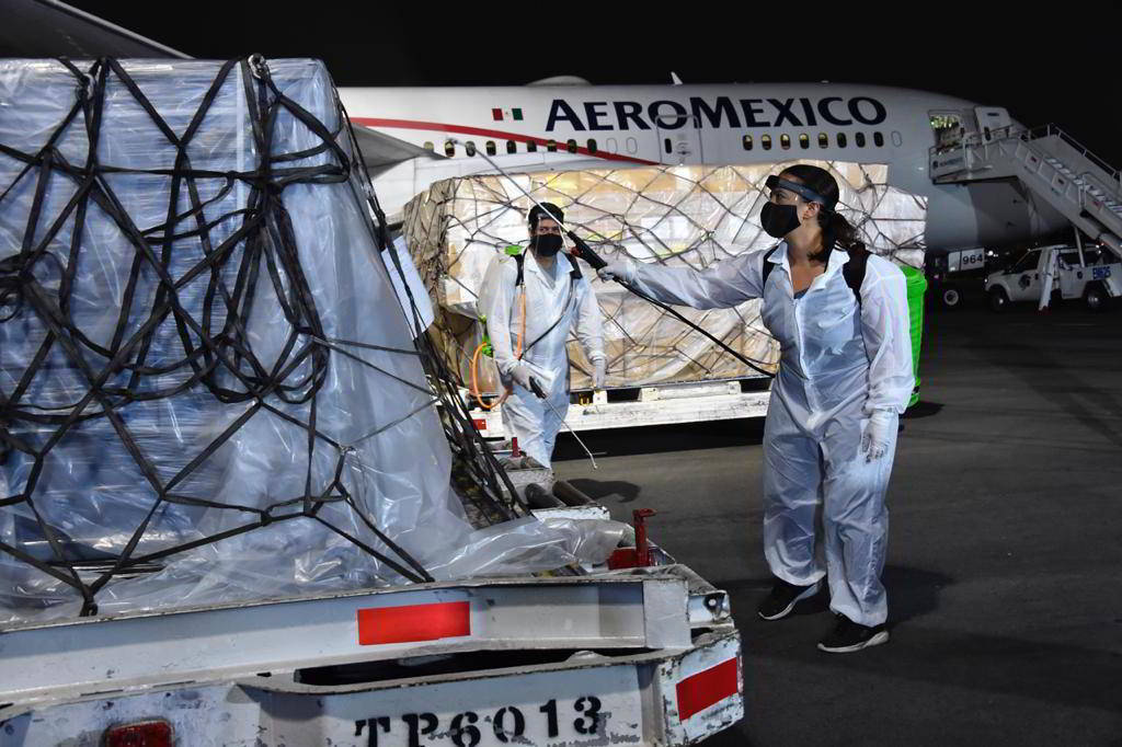 Personal con aspersores desinfectando contenedor al fondo un avión