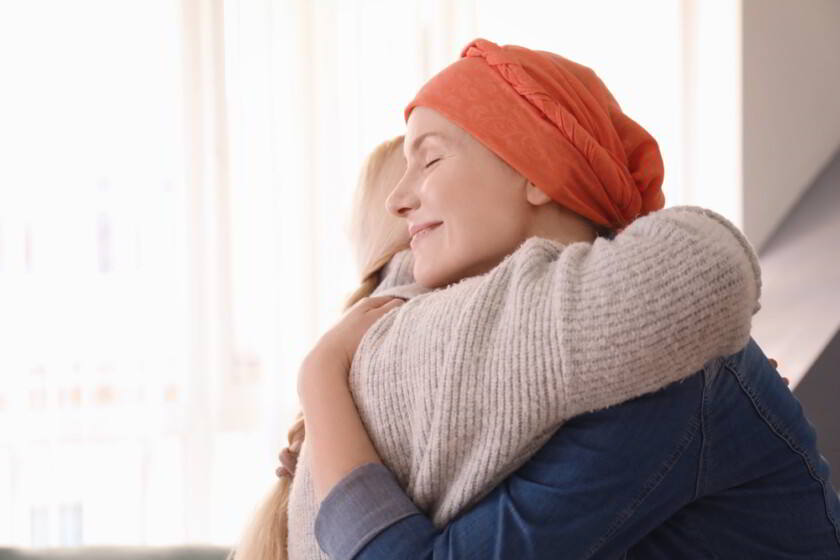 Mujer joven con cáncer abrazando a su madre en el interior